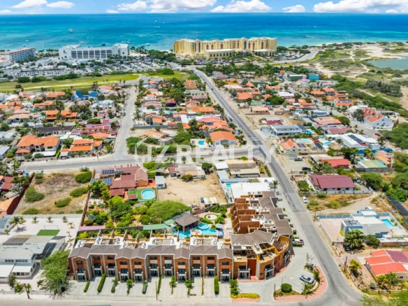 High aerial view of the Porta al Sole complex in Noord, Aruba, showing proximity to the high-rise hotels and the Caribbean Sea/Palm Beach area.