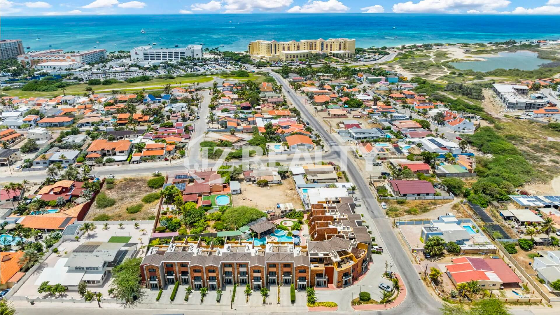High aerial view of the Porta al Sole complex in Noord, Aruba, showing proximity to the high-rise hotels and the Caribbean Sea/Palm Beach area.