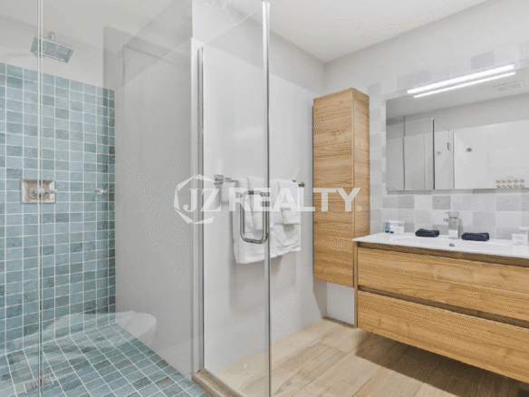Modern luxury bathroom at Porta al Sole Townhome in Aruba with wooden vanity and light blue/white mosaic tiled walk-in shower.