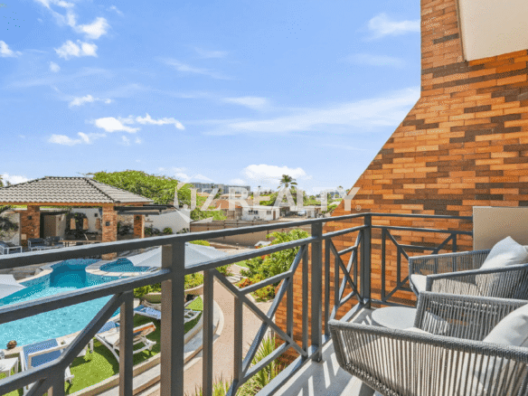 Balcony view from a Porta al Sole luxury residence, overlooking the resort-style swimming pool and beautifully landscaped community grounds in Noord, Aruba.