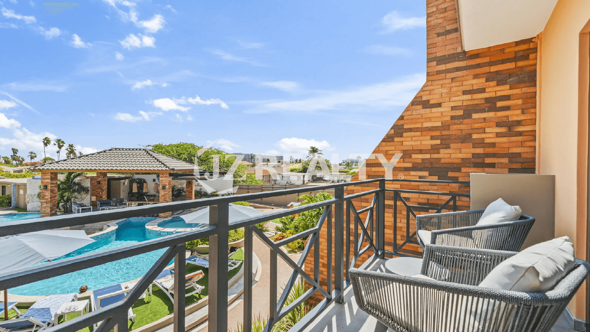 Balcony view from a Porta al Sole luxury residence, overlooking the resort-style swimming pool and beautifully landscaped community grounds in Noord, Aruba.