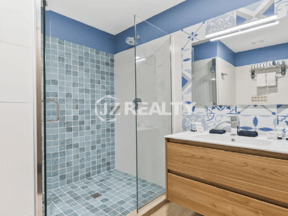 Guest bathroom at Porta al Sole Townhome with a wooden vanity, a large mirror, and a walk-in shower tiled in blue and white Mediterranean-style patterns.