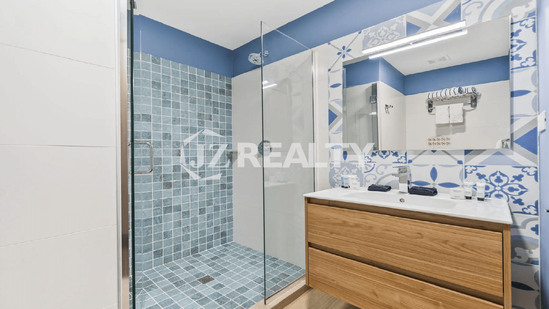 Guest bathroom at Porta al Sole Townhome with a wooden vanity, a large mirror, and a walk-in shower tiled in blue and white Mediterranean-style patterns.