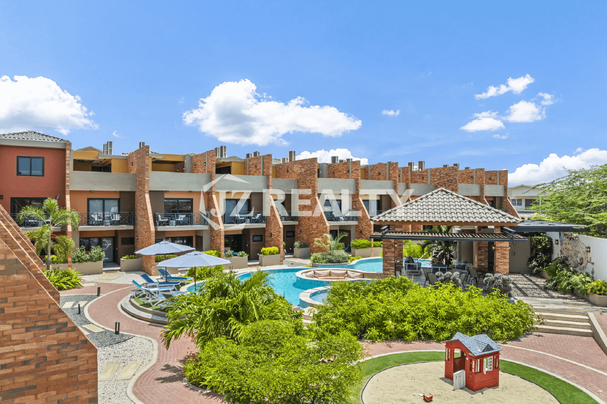 Aerial view of the Porta al Sole community buildings, complex pool, tropical landscaping, and a small children's play area.