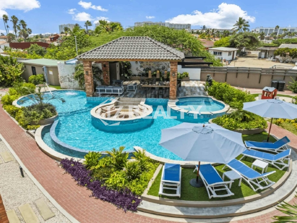Aerial view of the large community pool area with a fire pit, loungers, and tropical landscaping at Porta al Sole.