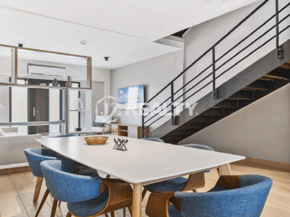 Modern dining area at Porta al Sole with a white table, blue upholstered chairs, and a contemporary open-riser staircase leading to the upper floors.