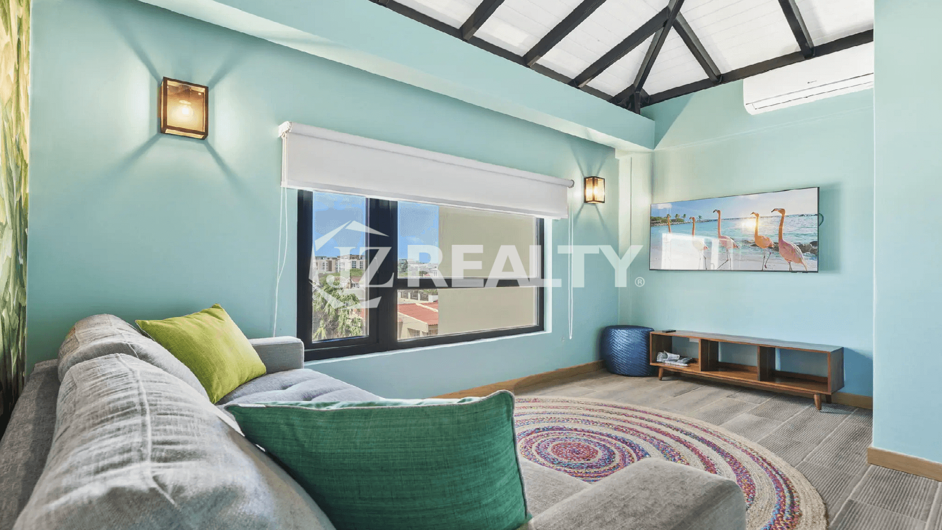 Upper-level family room/bonus room at Porta al Sole with vibrant teal walls, a vaulted ceiling, a large window, and a TV showing flamingos (Aruba wildlife).