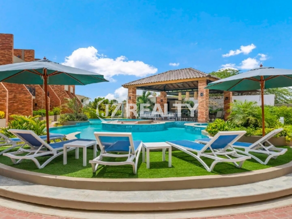 Resort-style community swimming pool at Porta al Sole, featuring sun loungers, umbrellas, and a central gazebo lounge area.