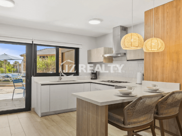 Ground-floor, fully-equipped modern kitchen at Porta al Sole with white cabinetry, a breakfast bar, and glass doors leading out to the patio and pool area.