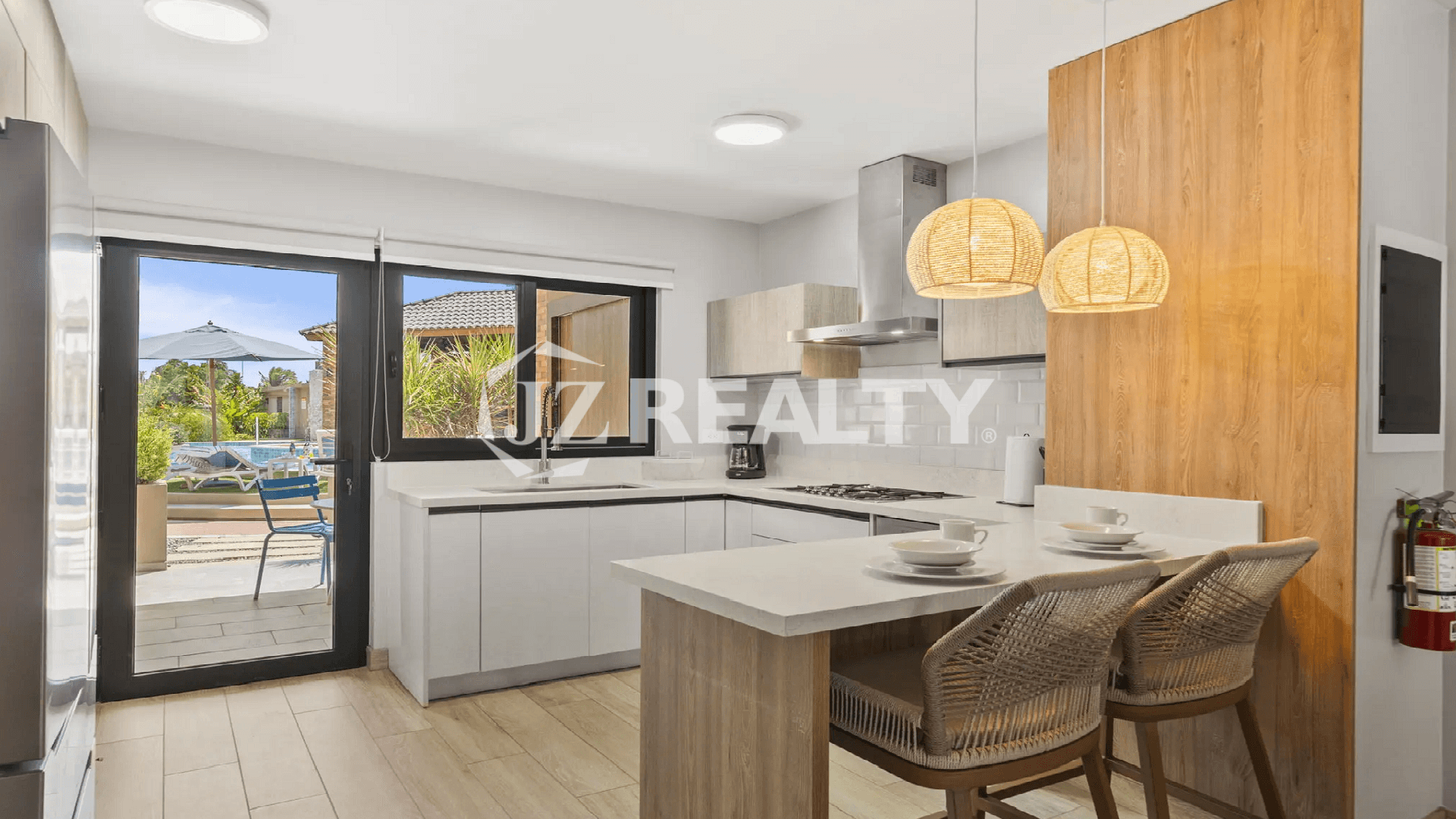 Ground-floor, fully-equipped modern kitchen at Porta al Sole with white cabinetry, a breakfast bar, and glass doors leading out to the patio and pool area.
