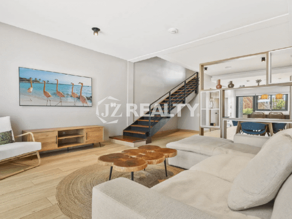 Bright, open-concept living room on the main floor of a Porta al Sole townhome, with a staircase, modern sectional sofa, and a natural wood coffee table.