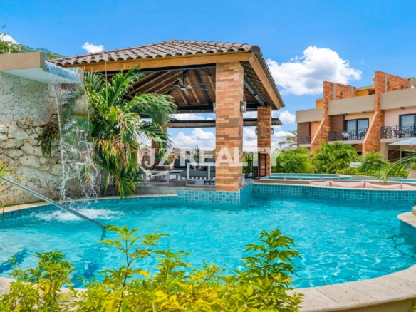 Close-up of the Porta al Sole community pool featuring a small rock waterfall, grotto, and lush tropical landscaping.
