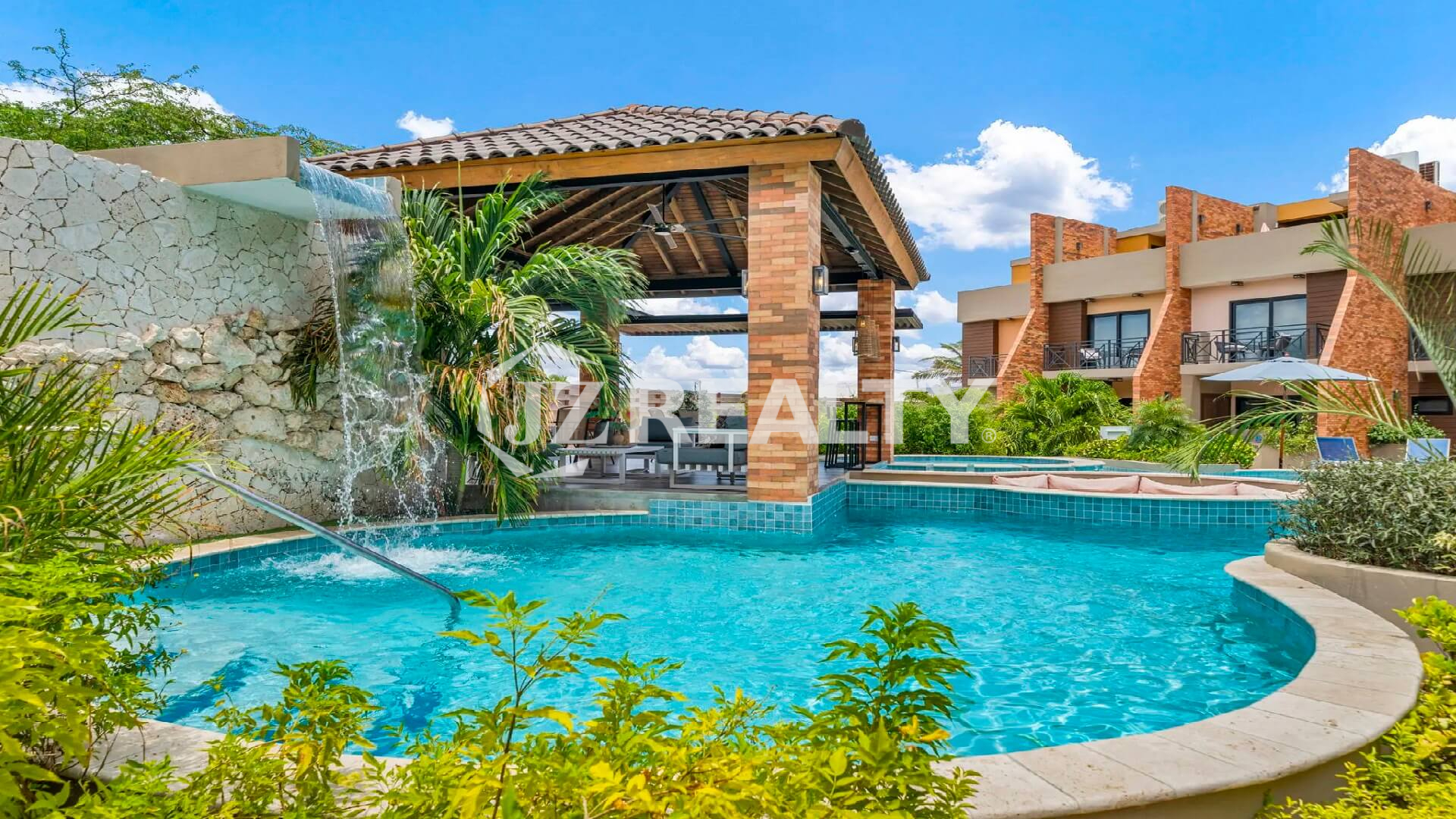 Close-up of the Porta al Sole community pool featuring a small rock waterfall, grotto, and lush tropical landscaping.