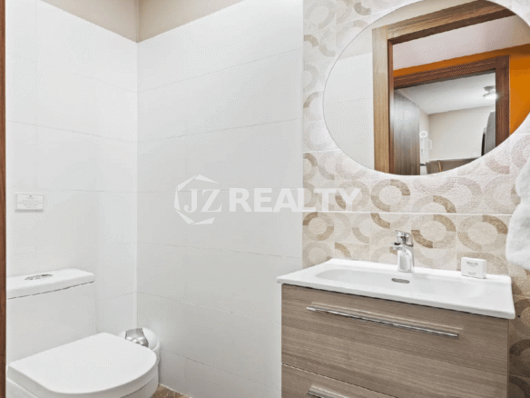 Ground-floor powder room or half bathroom at Porta al Sole with a modern wood-base vanity, round mirror, and patterned tile accent wall.