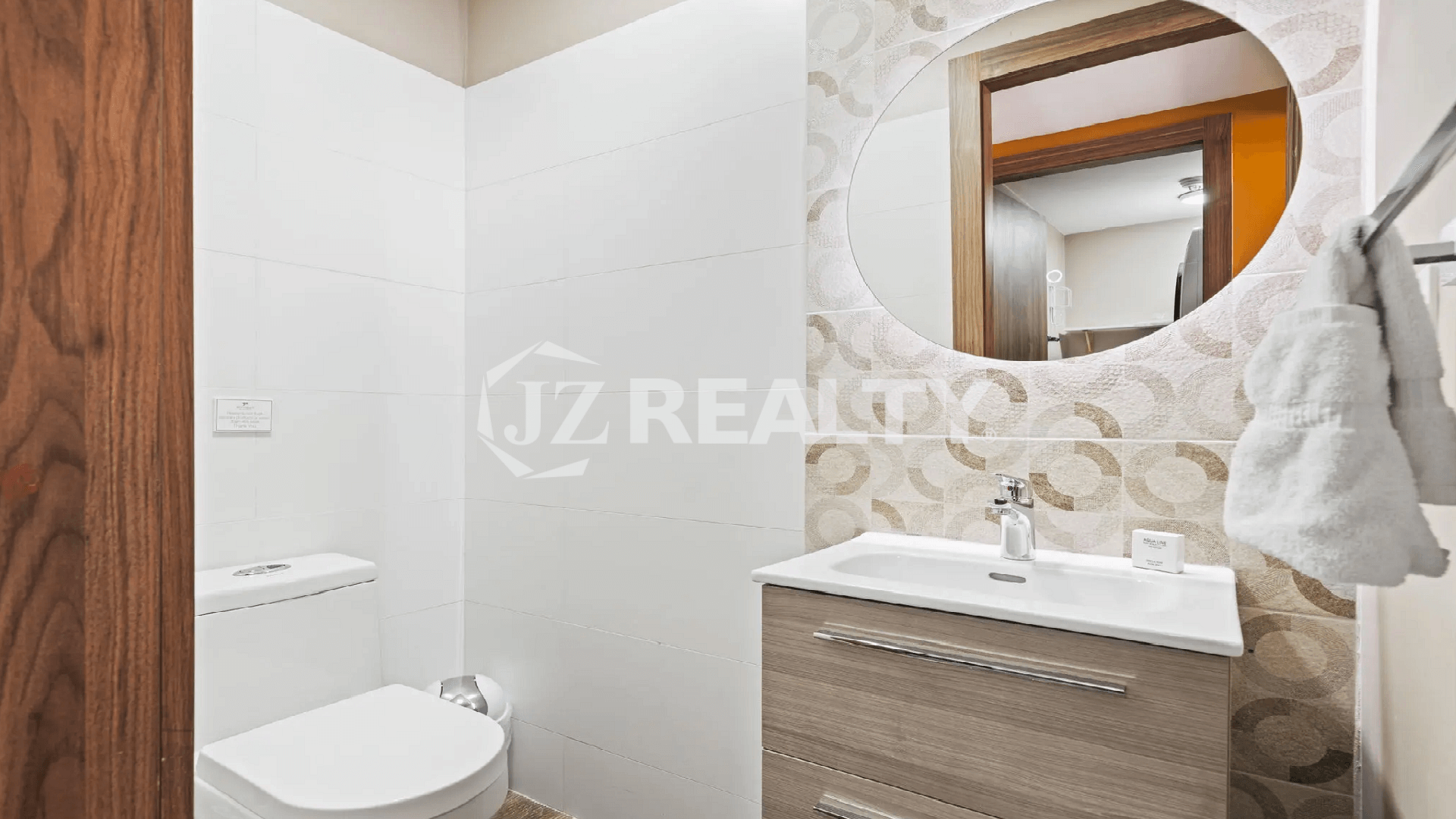 Ground-floor powder room or half bathroom at Porta al Sole with a modern wood-base vanity, round mirror, and patterned tile accent wall.