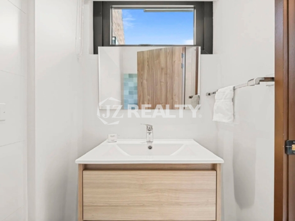 Ground floor half bathroom/powder room featuring a simple modern vanity with a light wood front and a window for natural light.