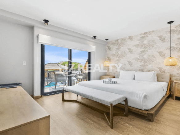 King-size primary bedroom at Porta al Sole, Noord, Aruba, featuring tropical leaf wallpaper, modern lighting, and sliding doors to a private balcony.