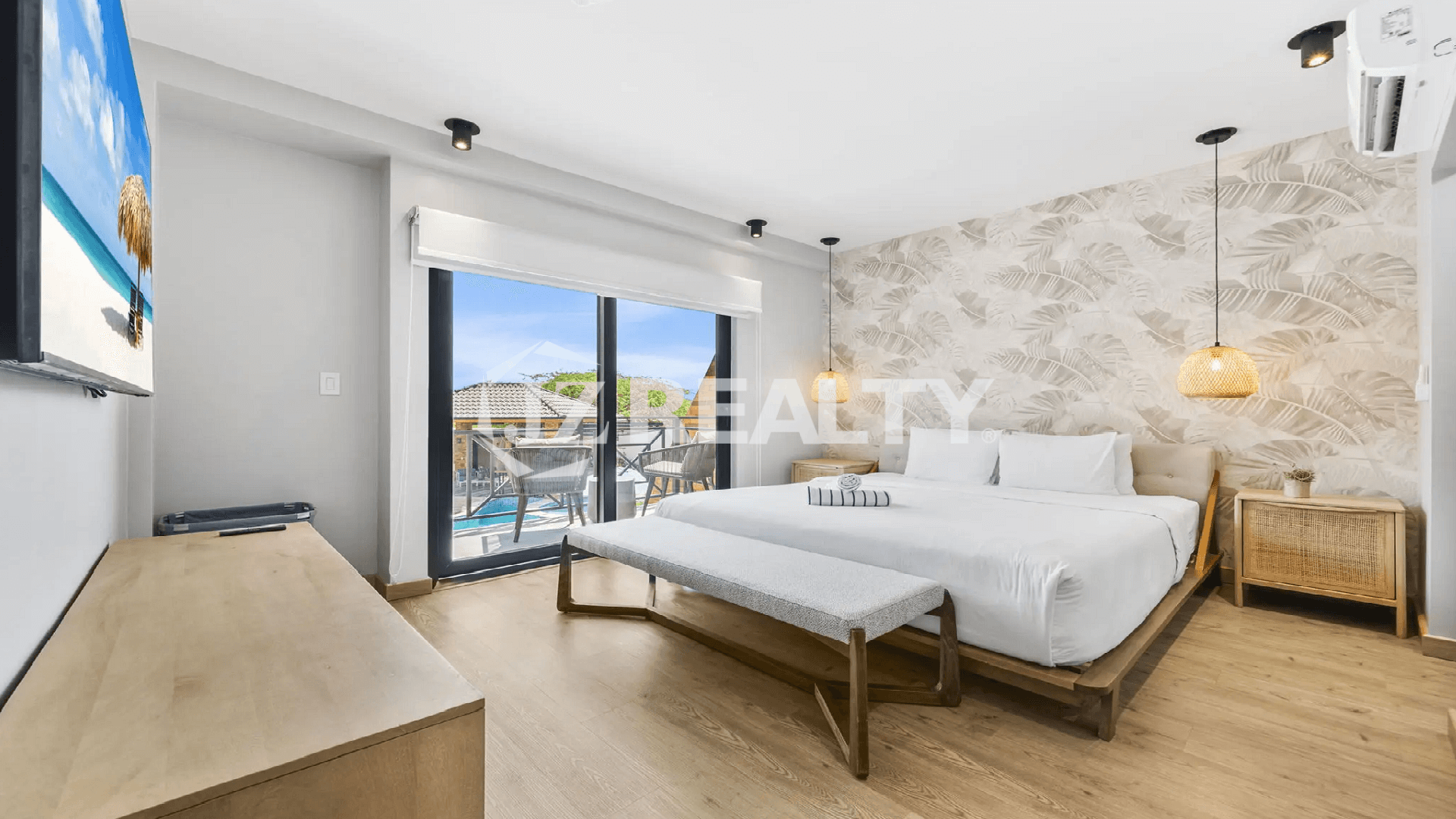 King-size primary bedroom at Porta al Sole, Noord, Aruba, featuring tropical leaf wallpaper, modern lighting, and sliding doors to a private balcony.
