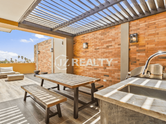 Private rooftop deck at Porta al Sole Townhouse with a shaded pergola, built-in BBQ/wet bar, outdoor dining table, and brick accent walls in Aruba.