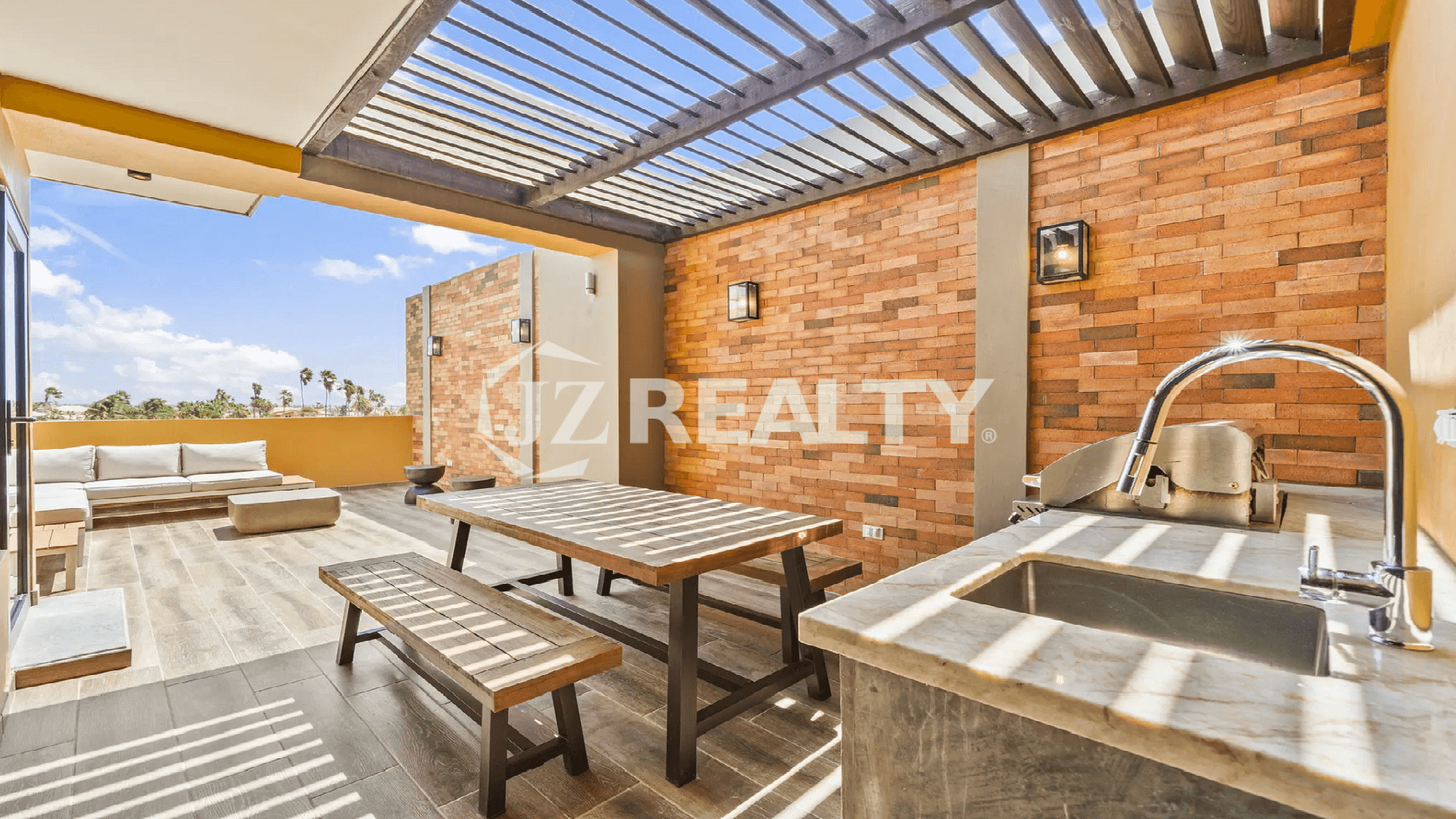 Private rooftop deck at Porta al Sole Townhouse with a shaded pergola, built-in BBQ/wet bar, outdoor dining table, and brick accent walls in Aruba.