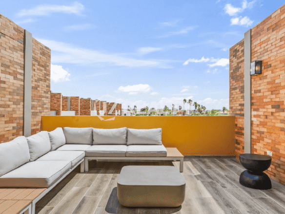 Rooftop terrace lounge area at the Porta al Sole Townhome in Aruba, featuring a large grey sectional sofa, modern side tables, and sunset views.
