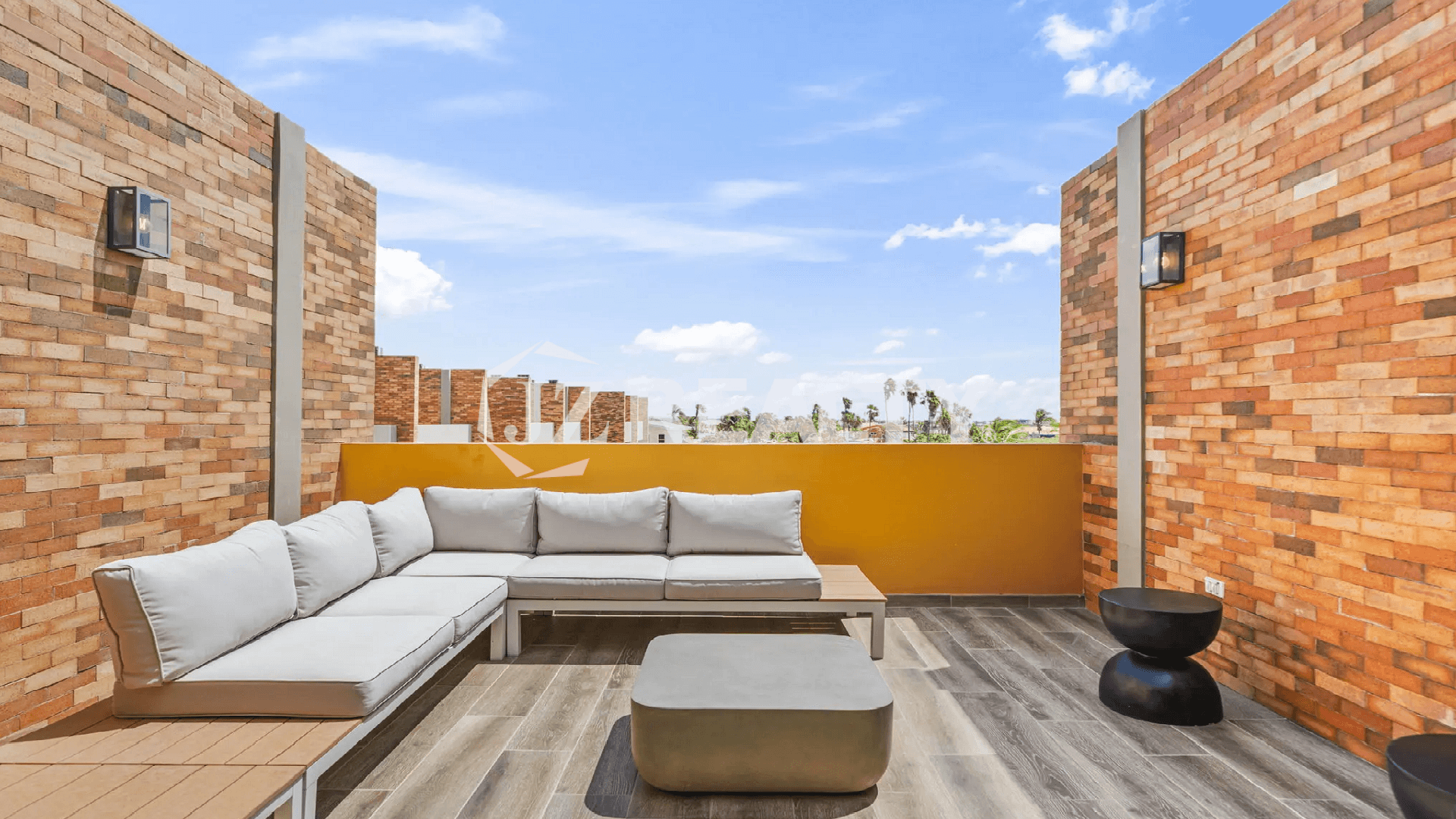 Rooftop terrace lounge area at the Porta al Sole Townhome in Aruba, featuring a large grey sectional sofa, modern side tables, and sunset views.