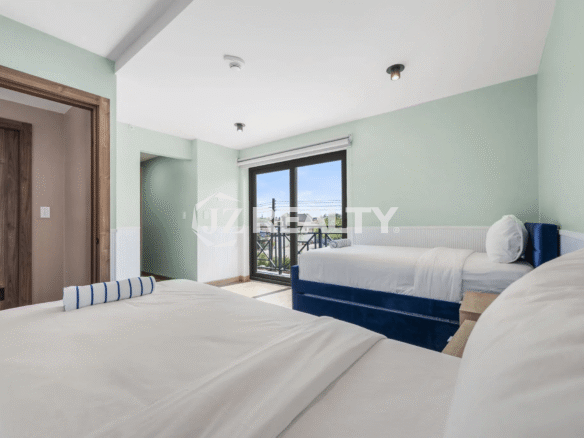 Bright bedroom in Porta al Sole Unit 12 with light green walls, two beds with white linens, and sliding glass doors leading to a private balcony.