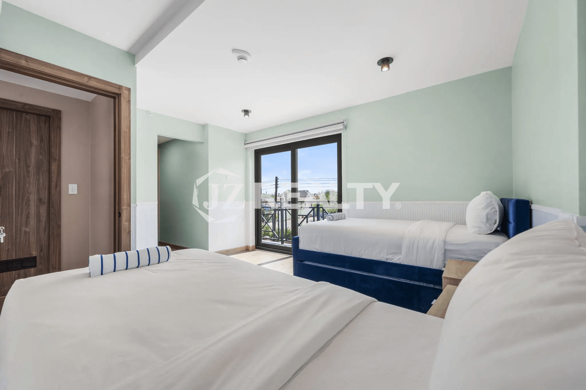 Bright bedroom in Porta al Sole Unit 12 with light green walls, two beds with white linens, and sliding glass doors leading to a private balcony.