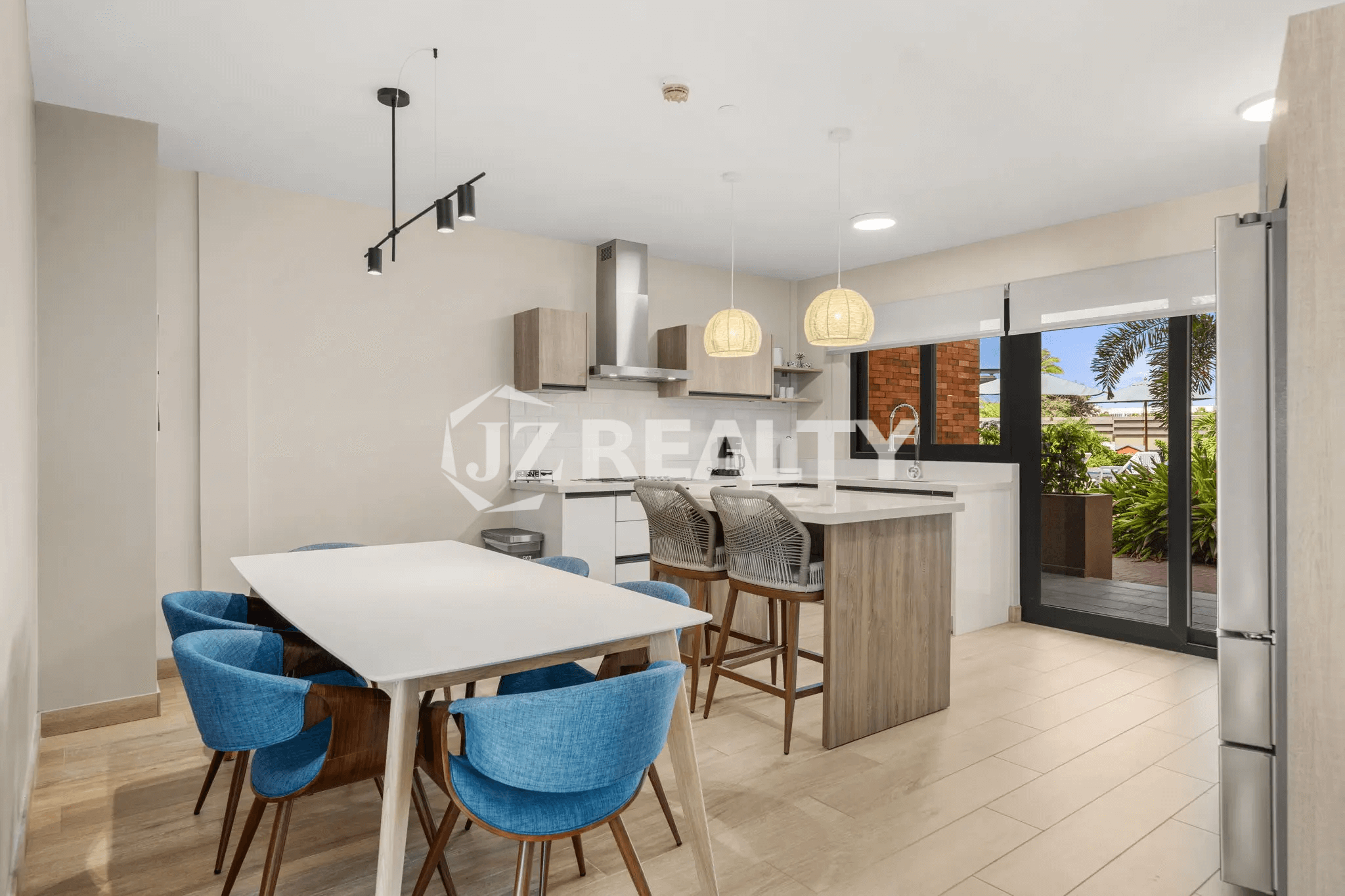 Dining area in Porta al Sole Unit 12 with a large white table and blue chairs, adjacent to the modern kitchen with a center island and view to the outdoor patio.