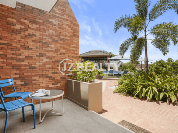 Private ground-floor patio area of Porta al Sole Unit 12 with a brick wall backdrop, outdoor table and blue chairs, and tropical planter box.
