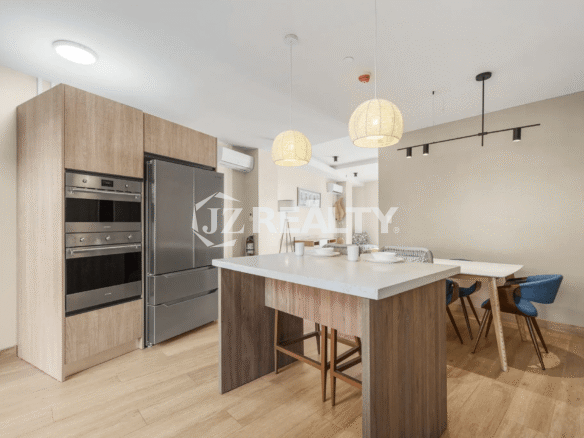 Corner view of the open-concept kitchen and dining area in Porta al Sole Unit 12, showcasing a stainless steel refrigerator, built-in ovens, and a kitchen island with seating.