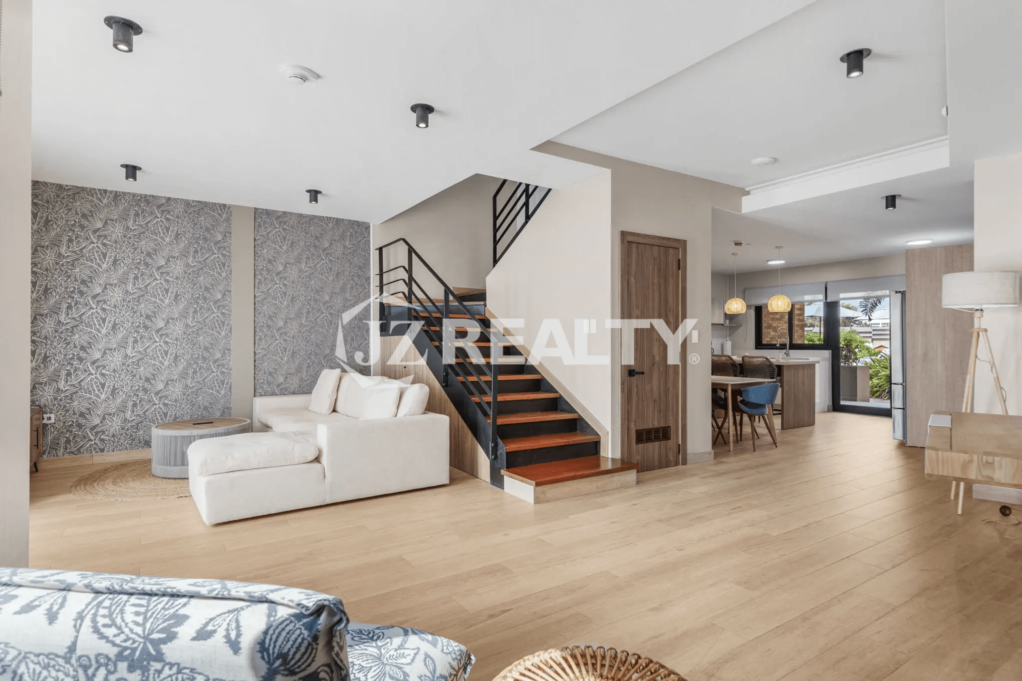 Open-plan living area in Porta al Sole Unit 12 with light wood flooring, a white sectional sofa, decorative wall paneling, and an open modern staircase leading to the second floor.