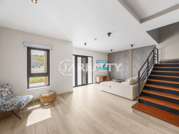 Open-concept living room in Porta al Sole Unit 12 showcasing light wood-look flooring, a large window, and a modern staircase with wood treads and a black metal railing leading to the upper floors.