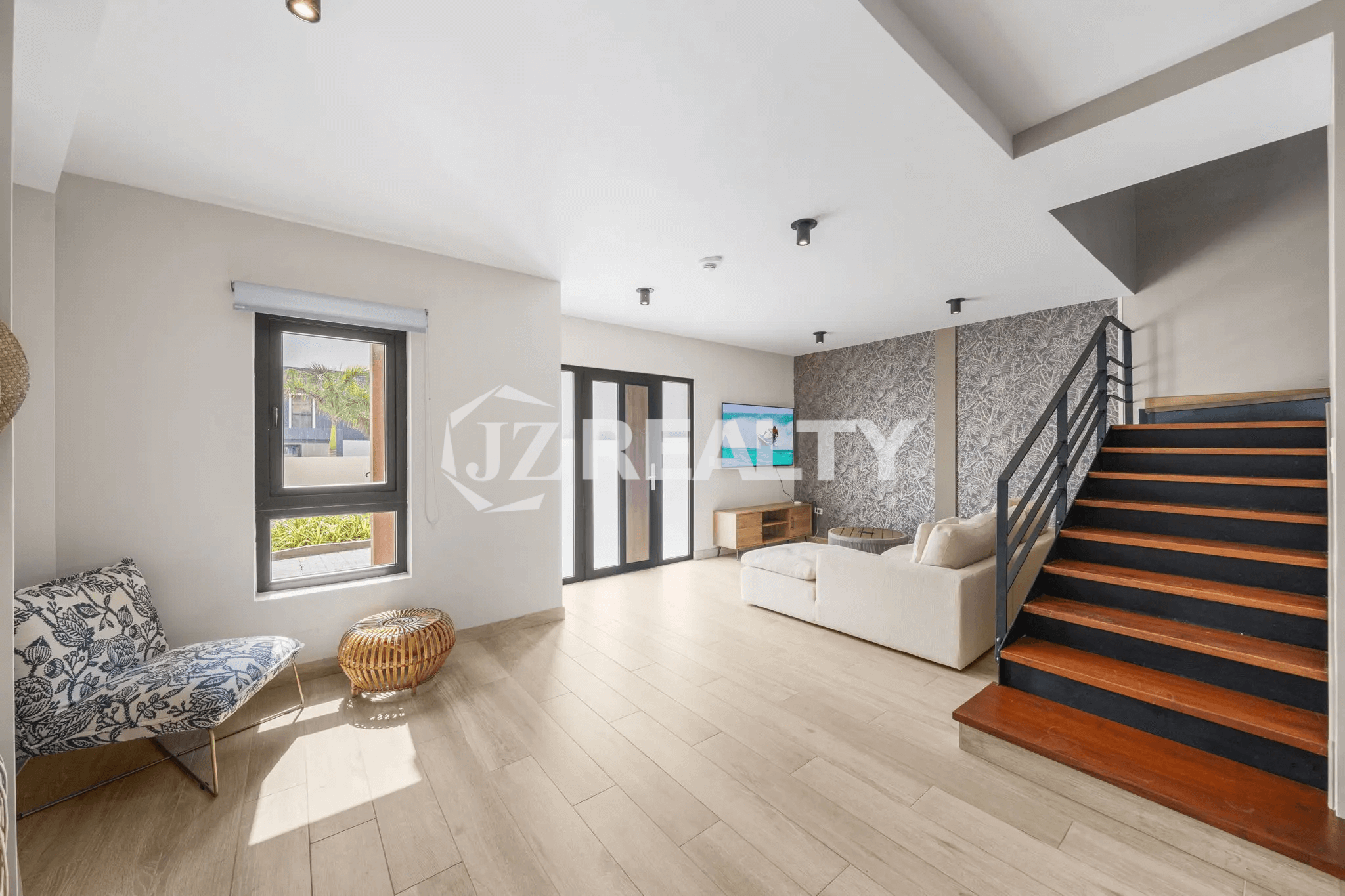 Open-concept living room in Porta al Sole Unit 12 showcasing light wood-look flooring, a large window, and a modern staircase with wood treads and a black metal railing leading to the upper floors.