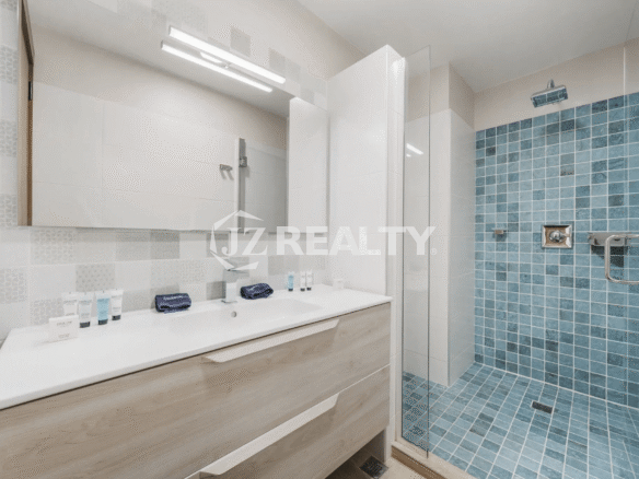 Contemporary bathroom in Porta al Sole Unit 12 with a light wood vanity, dual sinks, large mirror, and a spacious walk-in shower with blue mosaic tile and glass enclosure.