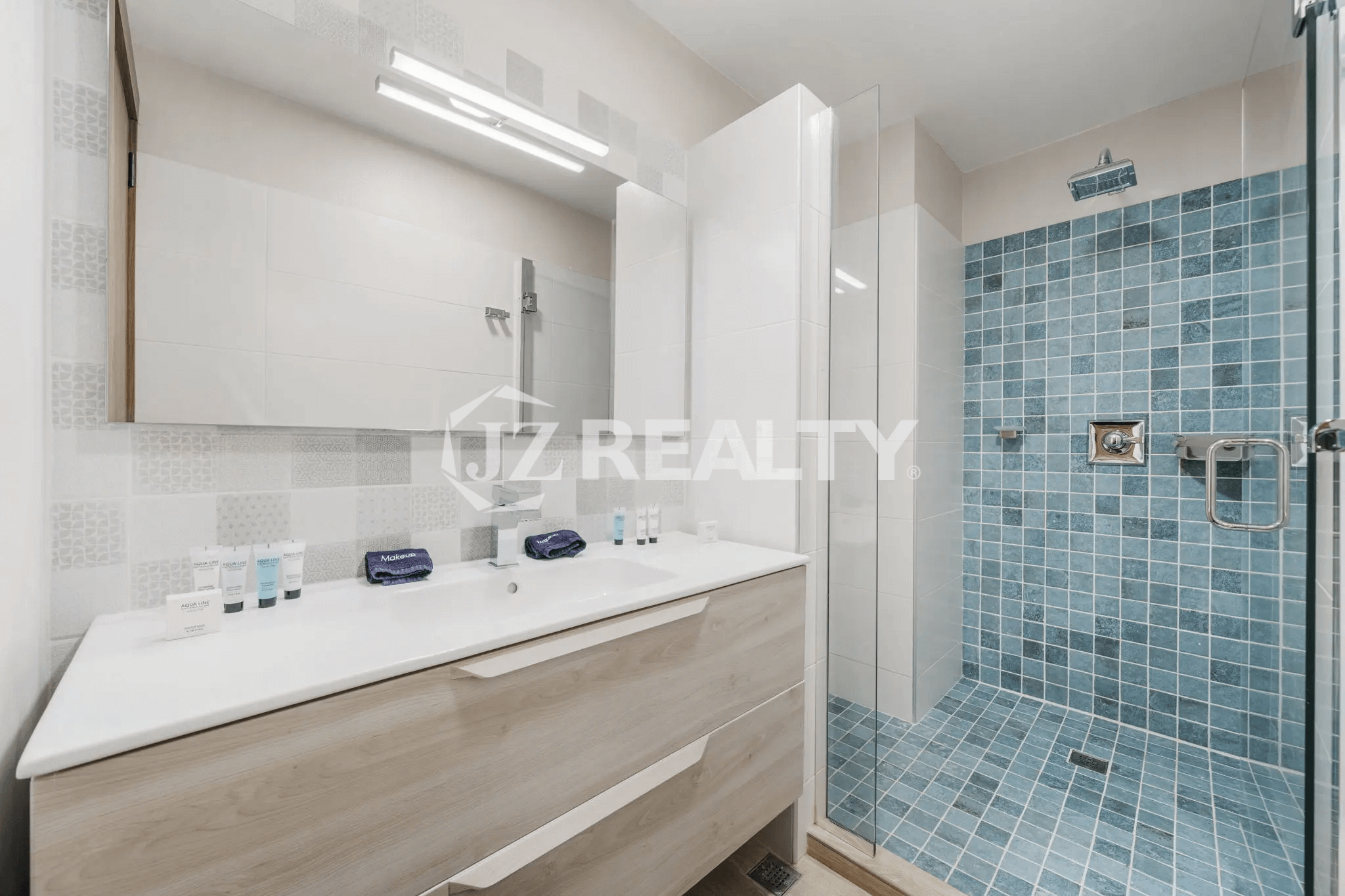 Contemporary bathroom in Porta al Sole Unit 12 with a light wood vanity, dual sinks, large mirror, and a spacious walk-in shower with blue mosaic tile and glass enclosure.