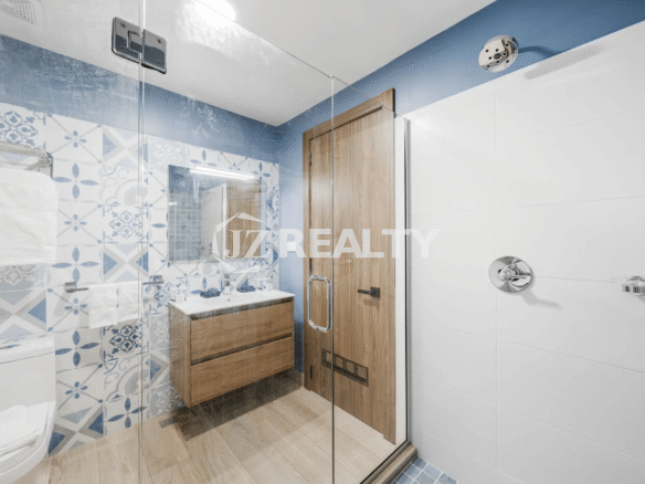 Bright and stylish bathroom in Porta al Sole Unit 12 with blue and white patterned accent tiles, a wooden vanity, and a separate glass-enclosed shower with white subway tiles.