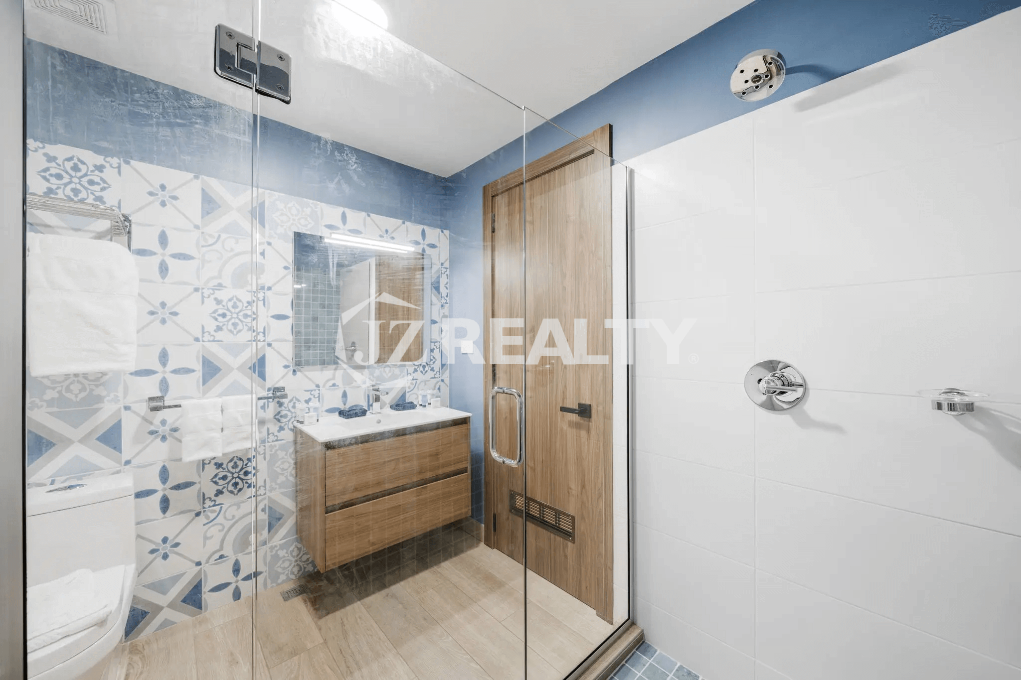 Bright and stylish bathroom in Porta al Sole Unit 12 with blue and white patterned accent tiles, a wooden vanity, and a separate glass-enclosed shower with white subway tiles.