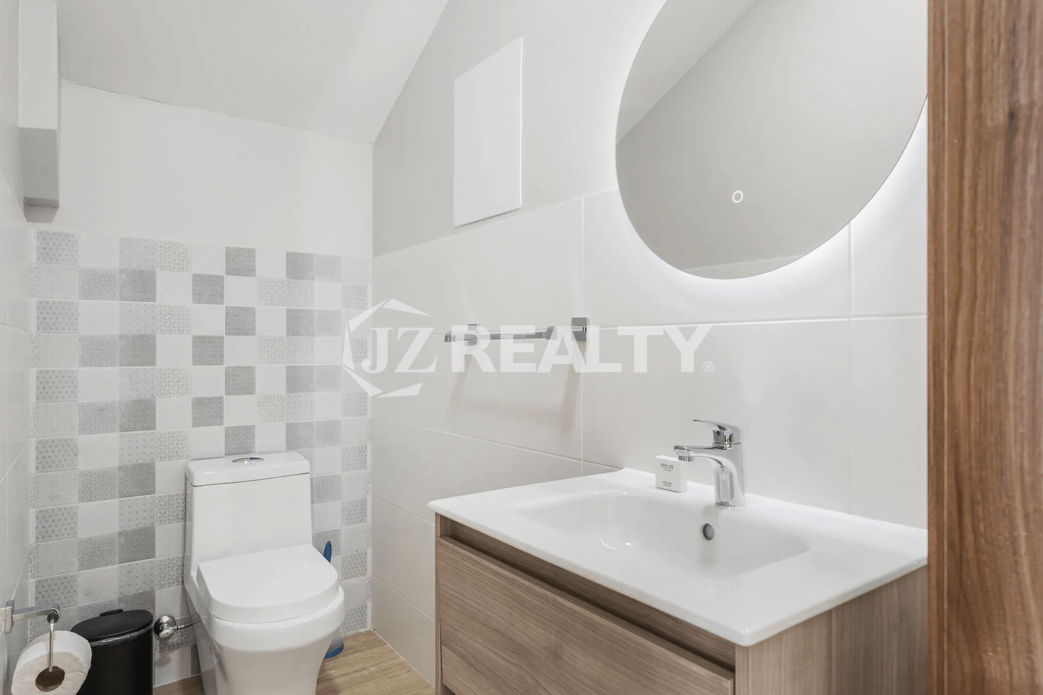Contemporary bathroom in Porta al Sole Unit 12 featuring a floating wooden vanity, white sink, backlit circular mirror, and patterned accent tile wall behind the toilet.