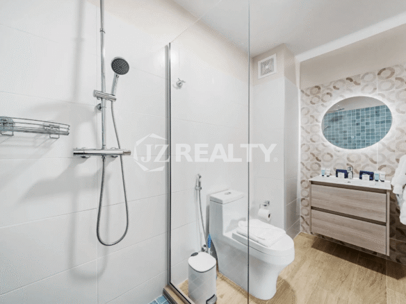 Modern bathroom in Porta al Sole Unit 12 featuring a glass-enclosed shower, wall-mounted shower system, white toilet, vanity with circular mirror, and white tiled walls.