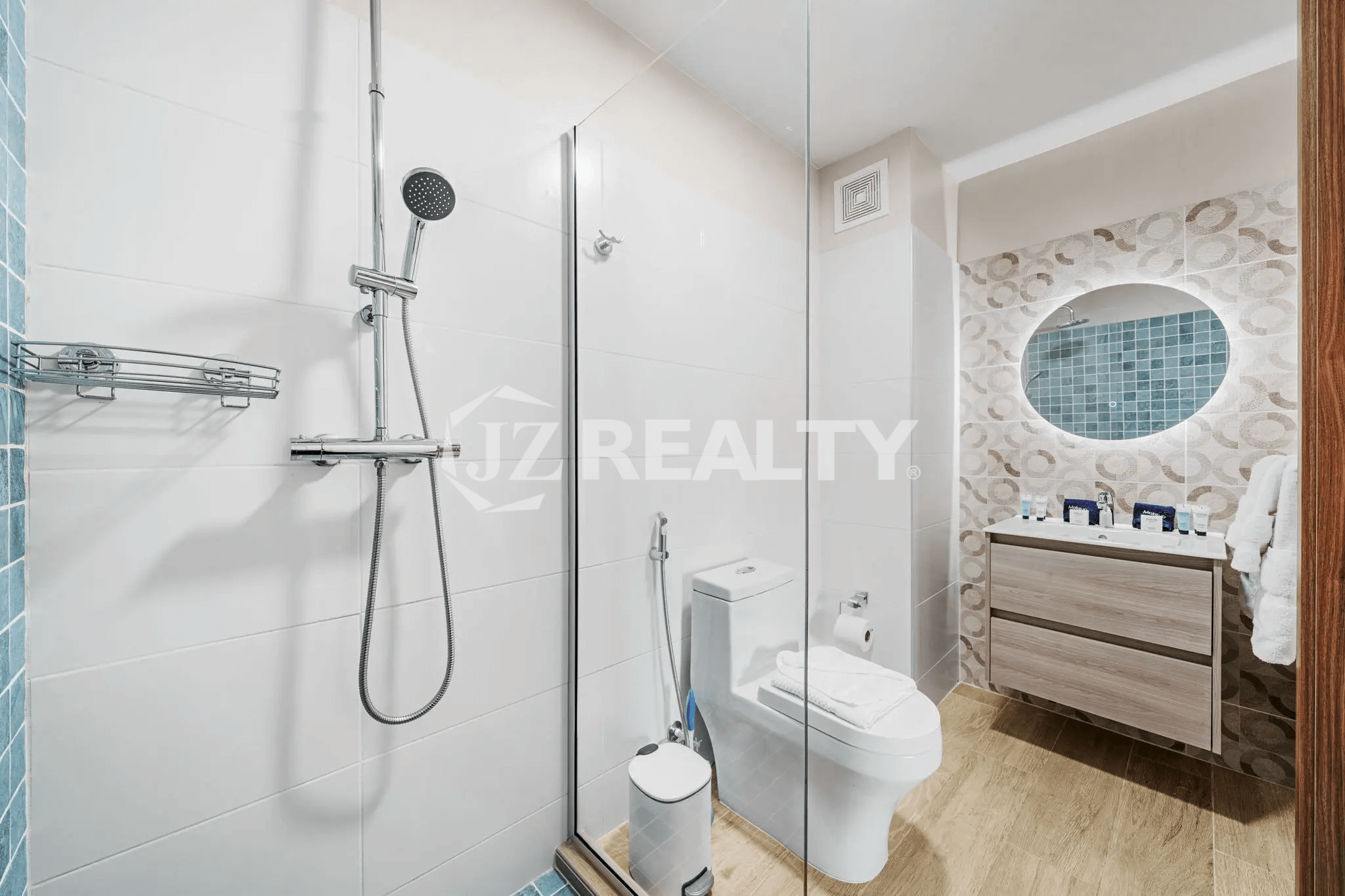 Modern bathroom in Porta al Sole Unit 12 featuring a glass-enclosed shower, wall-mounted shower system, white toilet, vanity with circular mirror, and white tiled walls.