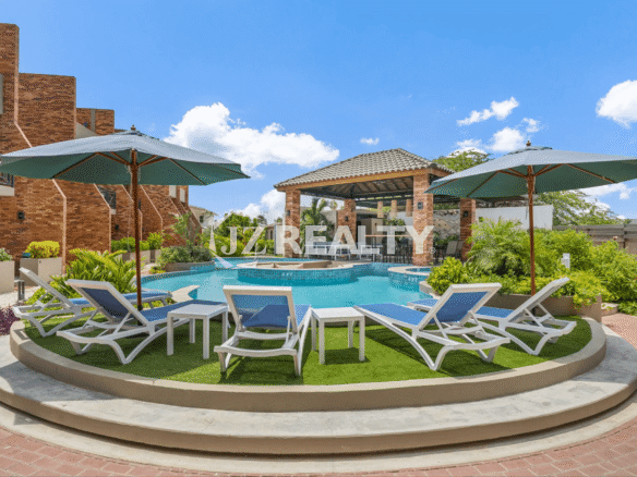 View of the main pool area at Porta al Sole, featuring comfortable sun loungers, tables, and umbrellas on a raised turf platform, with a central covered cabana.