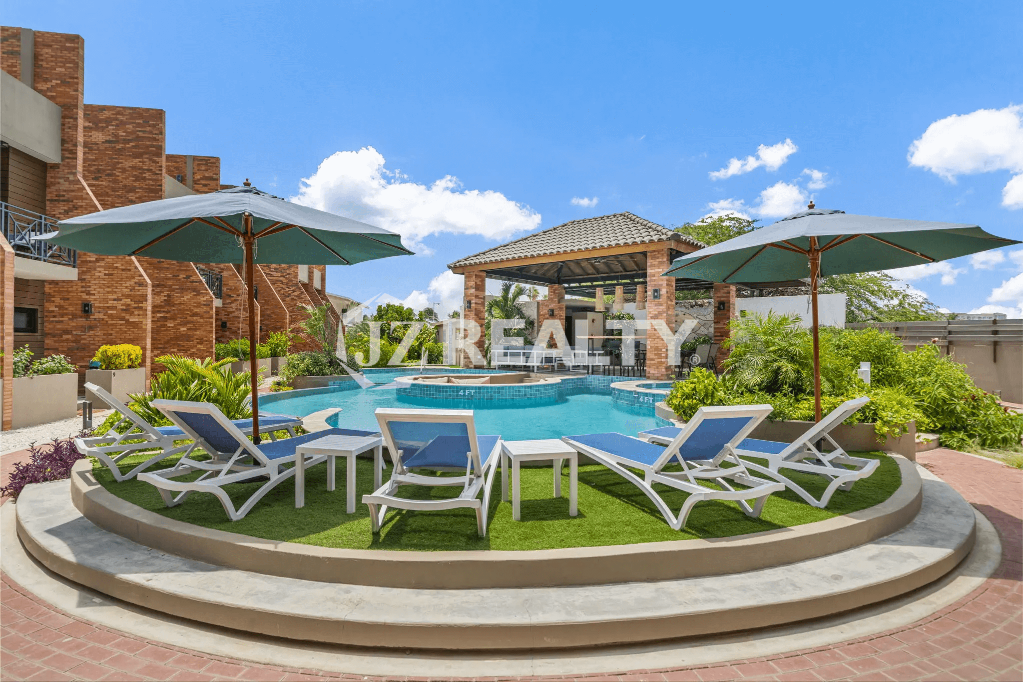 View of the main pool area at Porta al Sole, featuring comfortable sun loungers, tables, and umbrellas on a raised turf platform, with a central covered cabana.