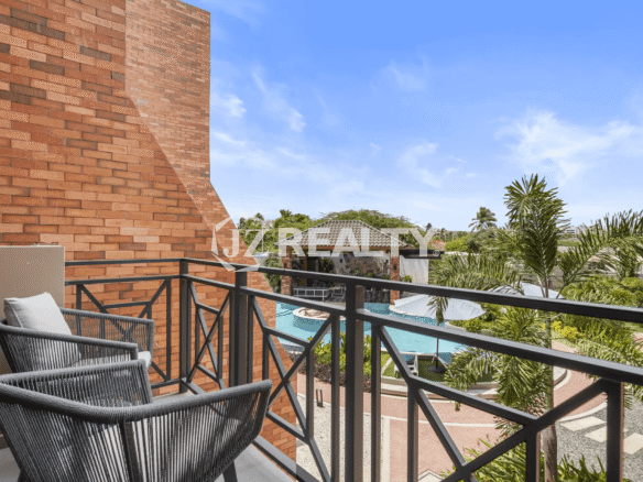 Balcony with outdoor seating at Porta al Sole Unit 12, offering a view over the complex's swimming pool, sun deck, and tropical surroundings.