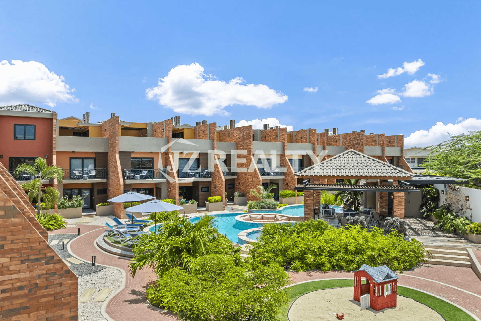 Aerial view of the lush, communal pool area at Porta al Sole, featuring a swimming pool, sun loungers, shaded cabana, and tropical landscaping.
