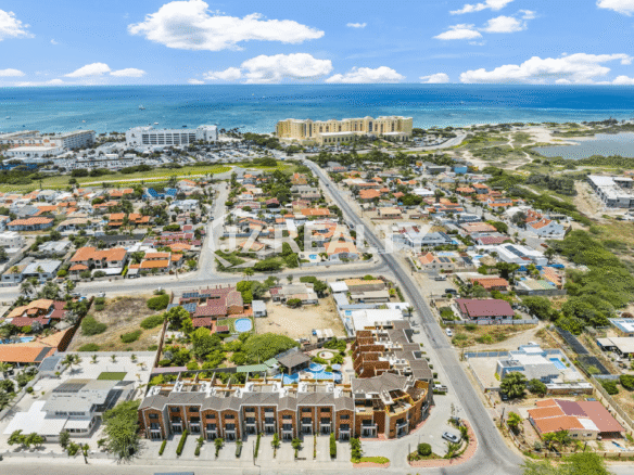 Aerial view of the Porta al Sole property and surrounding neighborhood, showing residential homes, the main road leading to high-rise hotels near the Caribbean Sea, and the ocean horizon.