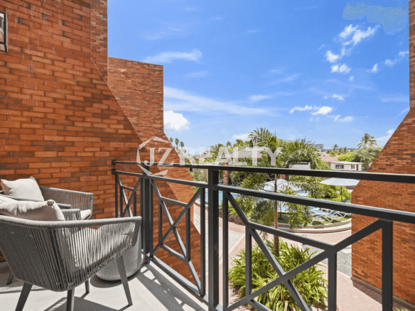 Balcony in Porta al Sole Unit 13 with two grey woven chairs, dark metal railing, overlooking a lush courtyard and neighborhood.