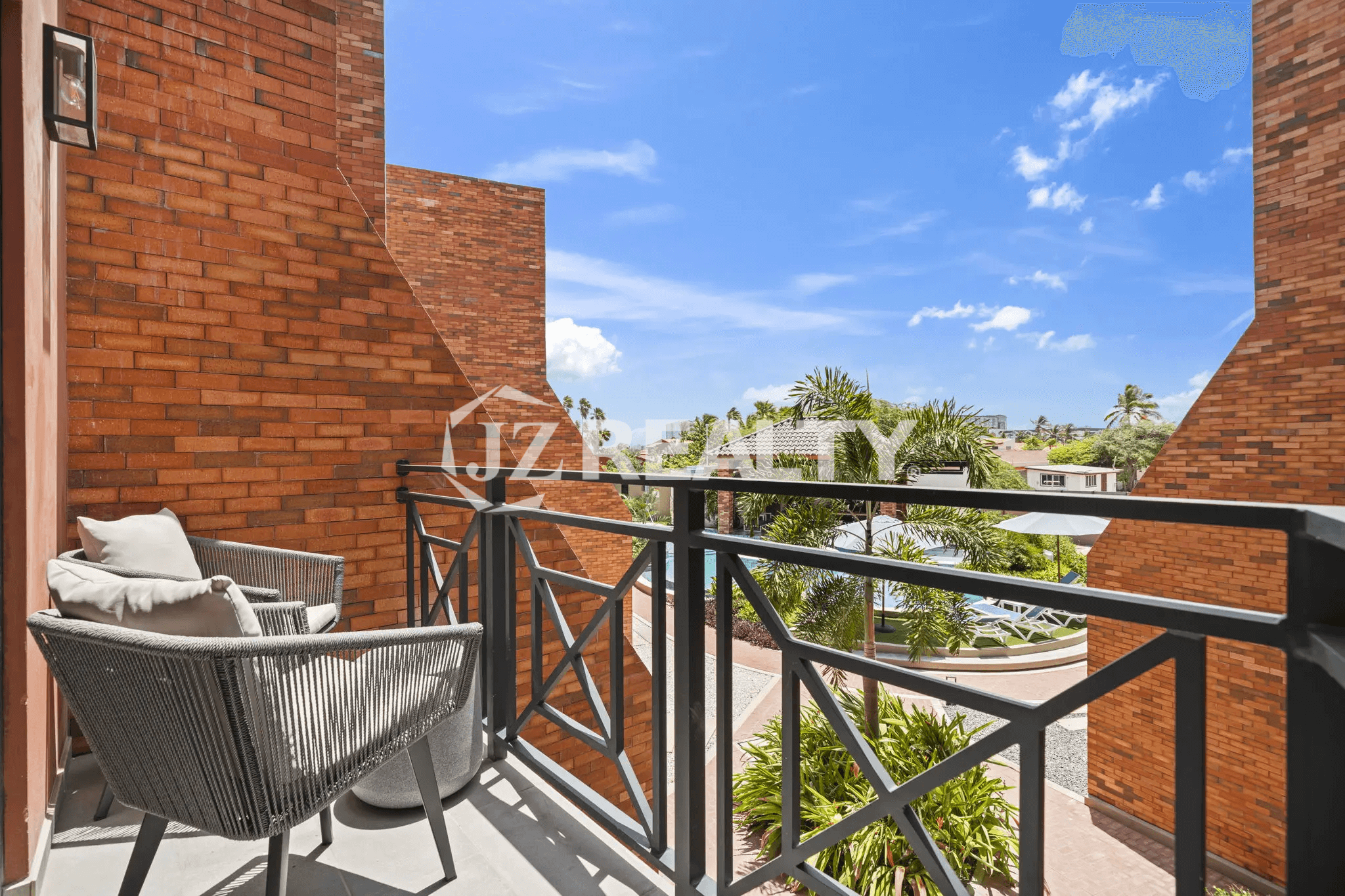 Balcony in Porta al Sole Unit 13 with two grey woven chairs, dark metal railing, overlooking a lush courtyard and neighborhood.