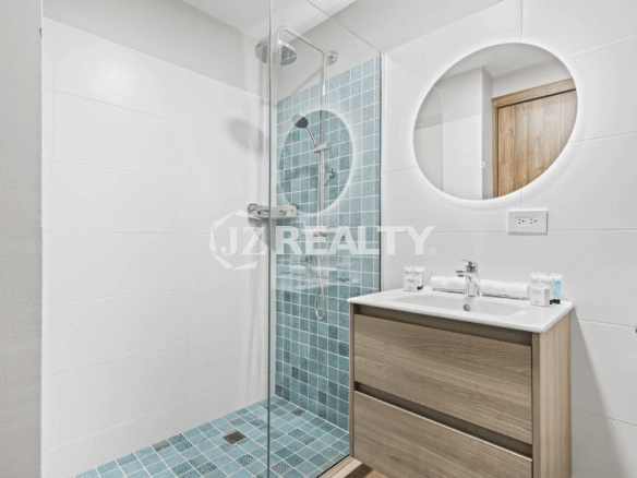 Modern bathroom in Porta al Sole Unit 13 with a glass shower enclosure, blue tiled shower wall and floor, wood vanity, and circular backlit mirror.