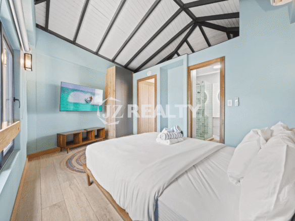 Bright bedroom in Porta al Sole Unit 13 with light blue walls, a dramatic vaulted white and black ceiling, king bed, and TV.
